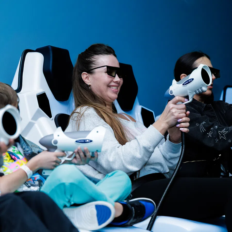 Group of people wearing 3D glasses playing interactive video games with light guns in a gaming lounge.