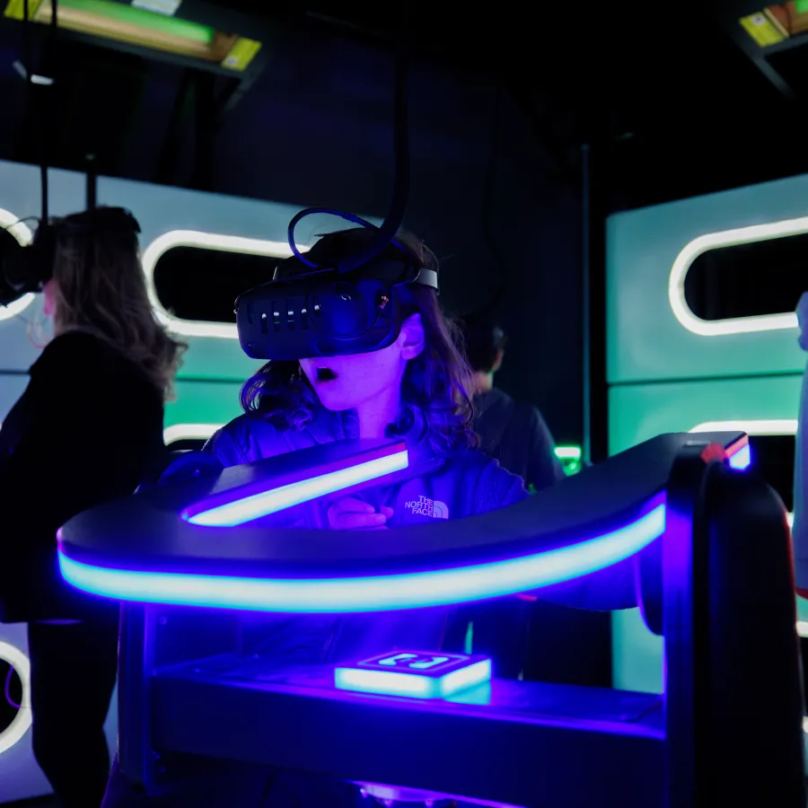People wearing virtual reality headsets interacting with neon-lit VR gaming stations in a dark room.