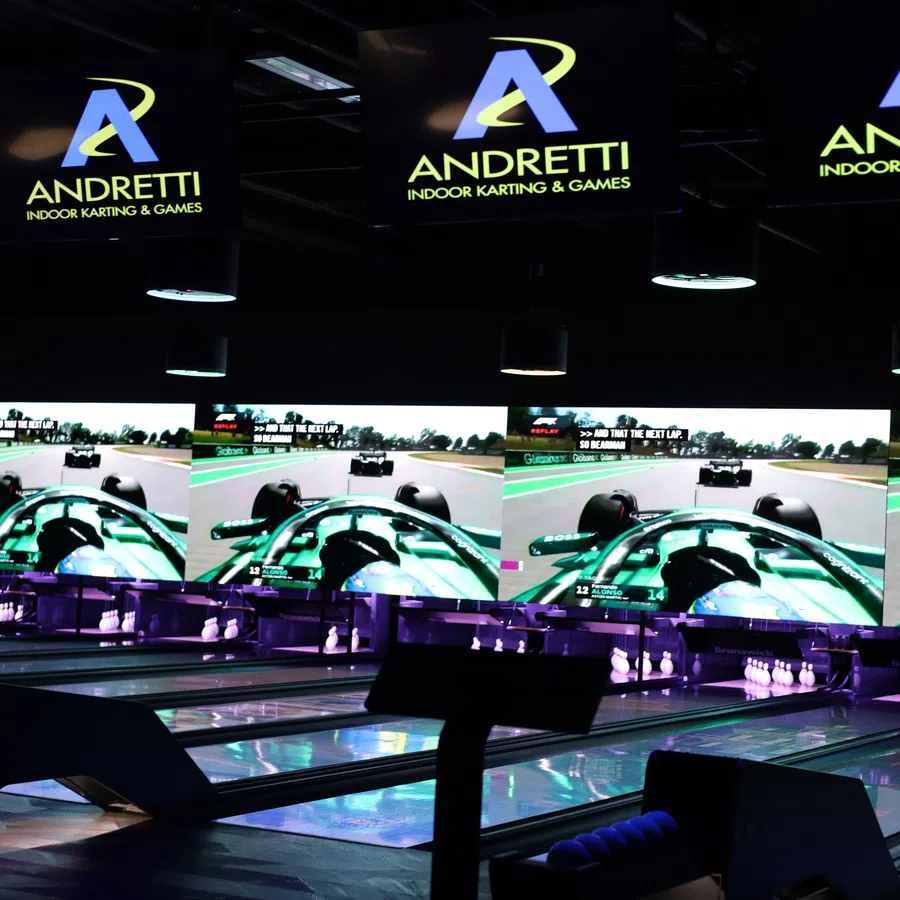 Andretti Indoor Karting & Games with bowling lanes and large screens displaying racing visuals in dark ambient lighting.