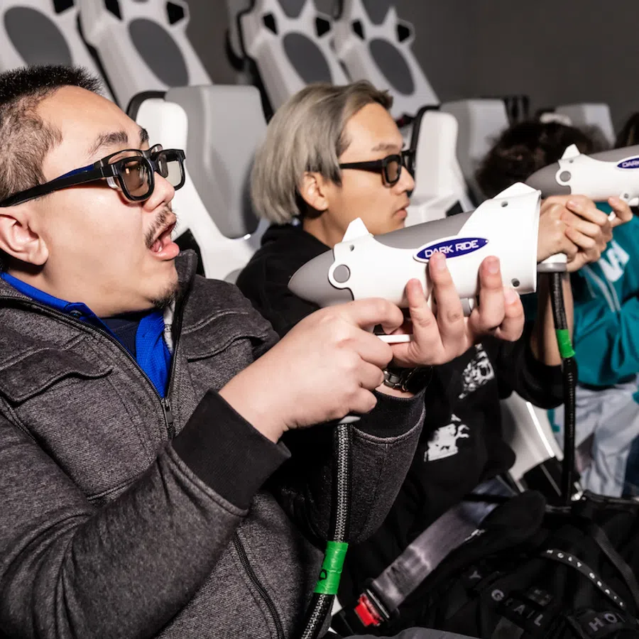 Group of people wearing 3D glasses playing an interactive shooting game in a dark entertainment venue.