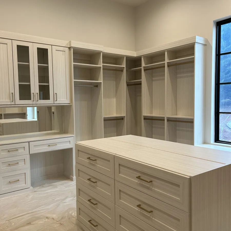 Spacious walk-in closet with light wood cabinets, drawers, shelves, hanging rods, and a window.