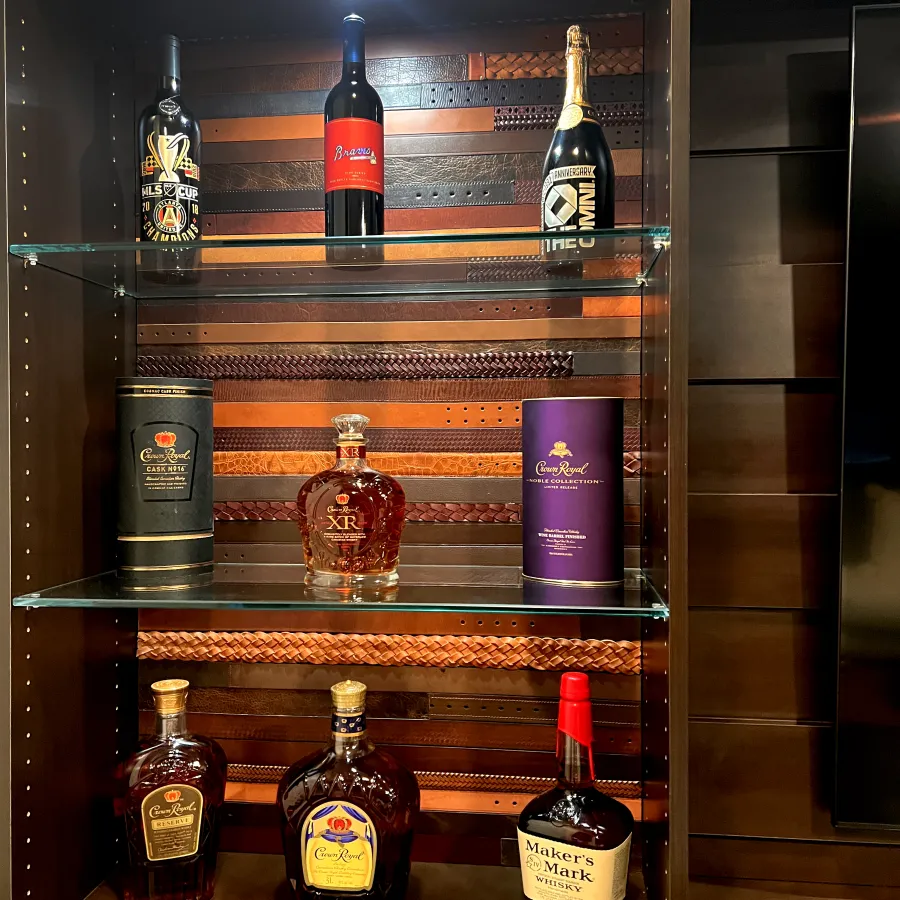 Close up of whisky bottles including Crown Royal and Maker's Mark bourbon on glass shelves with a wooden background in a whisky room