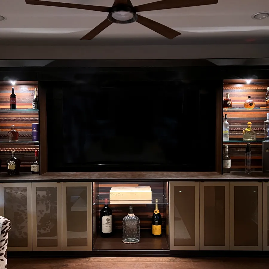 Custom designed whisky room with whisky bar and glass shelves, whisky bottles, glass cabinets, accent lighting, a large flat screen tv and a hardwood floor