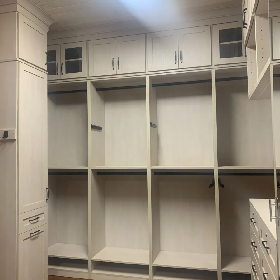 Empty white built-in closet organizer with shelves and drawers in a room with wooden floor.
