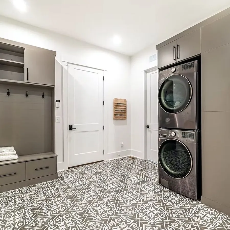 Modern laundry room with stacked washer and dryer, patterned tile floor, and gray built-in storage units.