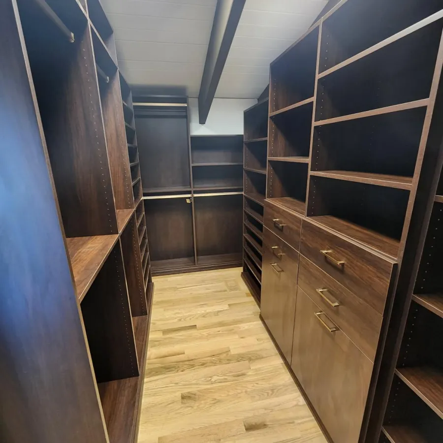 Spacious walk-in closet with dark wood shelves, drawers, and light hardwood flooring under skylights.