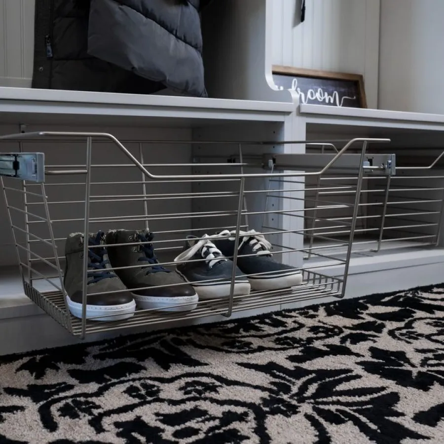 Organized entryway with pull-out wire basket storing shoes beneath a wall-mounted bench with cushions and coat hooks.