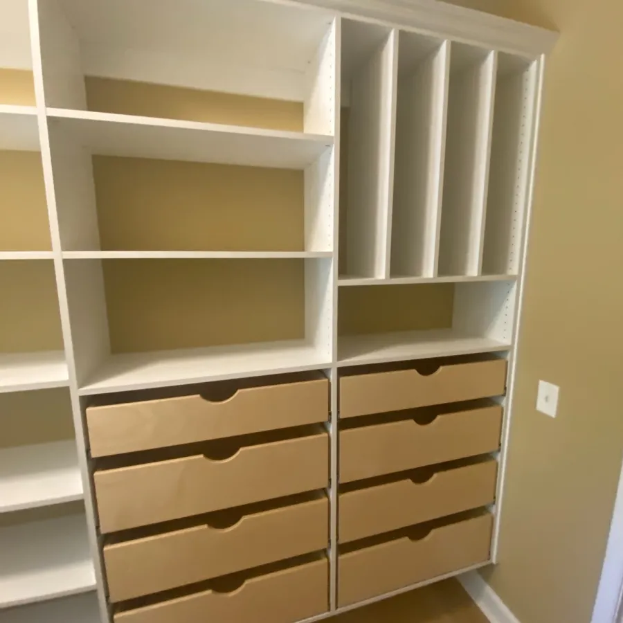 White shelving unit with multiple compartments and beige storage boxes on the right side in a room corner.