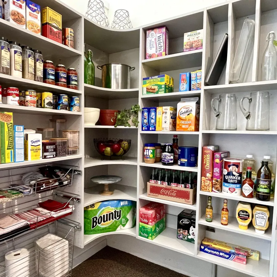 Custom designed kitchen pantry with white shelves stocked with canned goods, beverages, snacks and paper towels