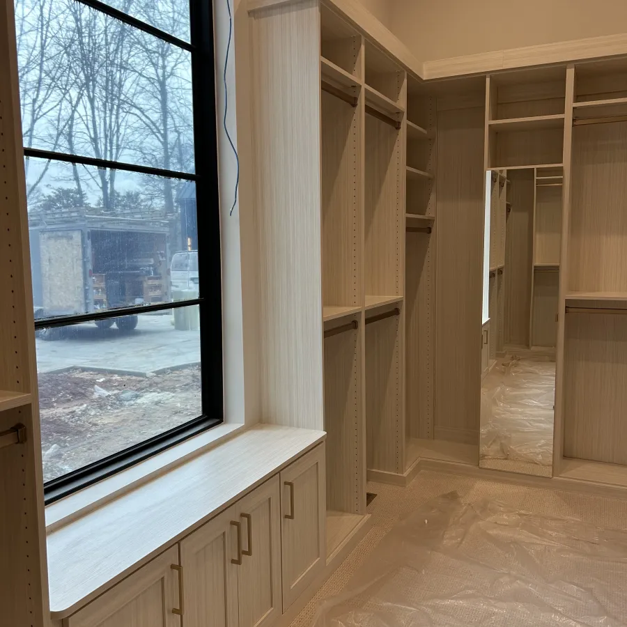 Light wood walk-in closet with shelves, hanging rods, a full-length mirror, and a window bench with storage cabinets.