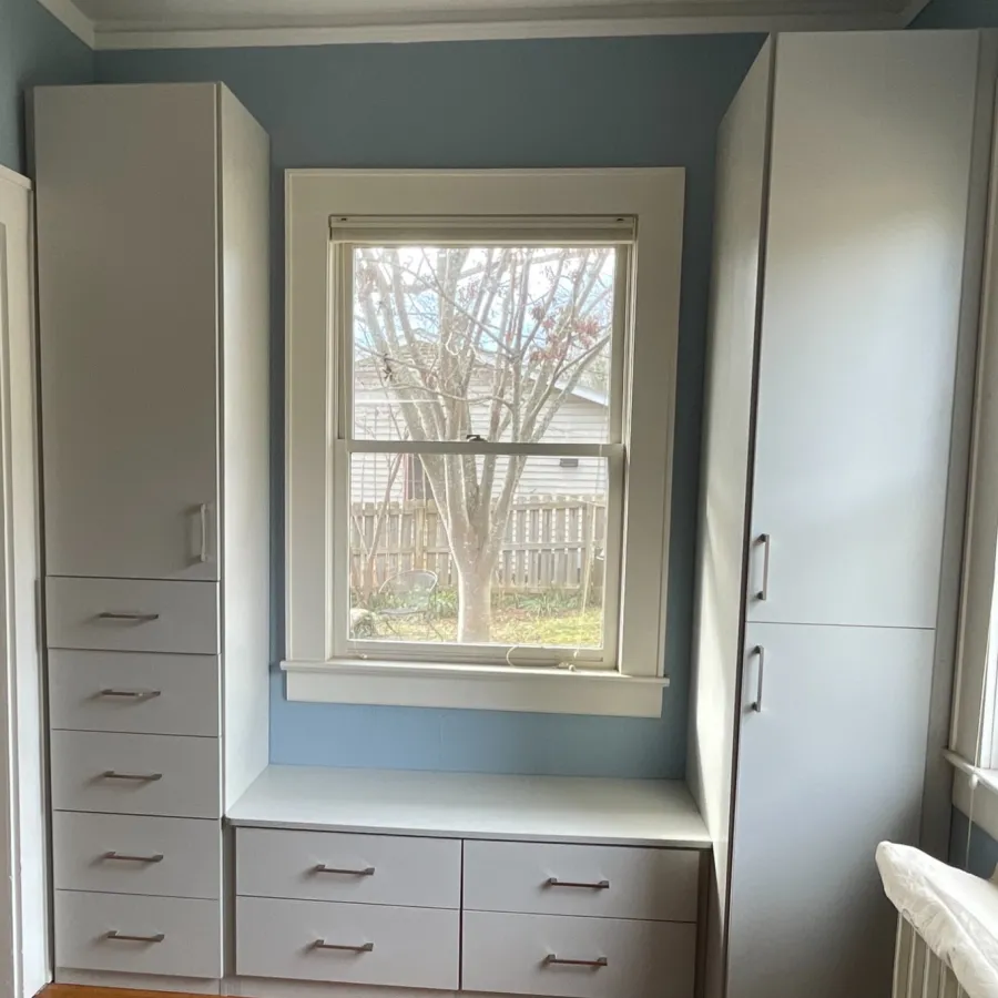 Built-in white cabinetry surrounding a window with light blue walls and hardwood flooring.