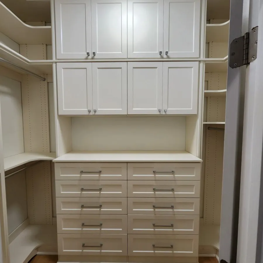 Organized white walk-in closet with multiple drawers, cabinets, shelves, and hanging rods on hardwood floors.