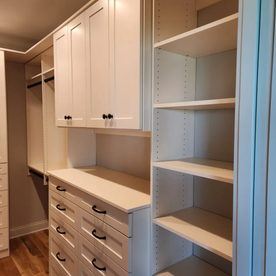 Organized walk-in closet with white cabinetry, multiple drawers, shelves, hanging rods, and wood flooring.