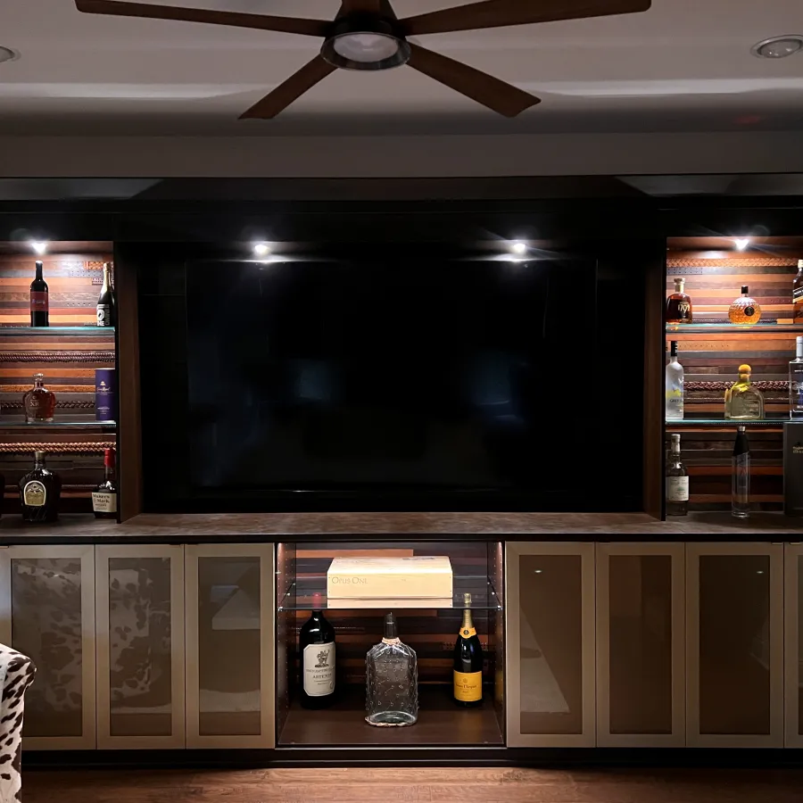 Custom designed whisky room with whisky bottles, decanters, glass shelves and cabinets and a large flat-screen TV.