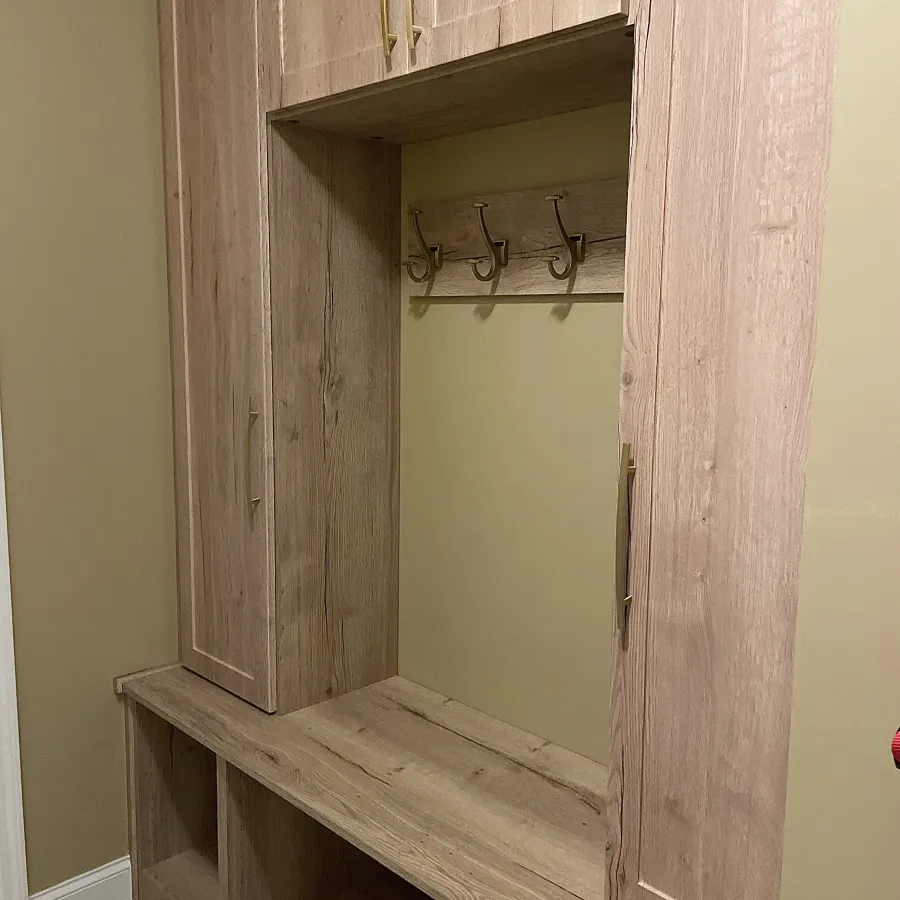 Wooden hallway storage bench with cabinets, open cubbies, and wall hooks for coats and bags.