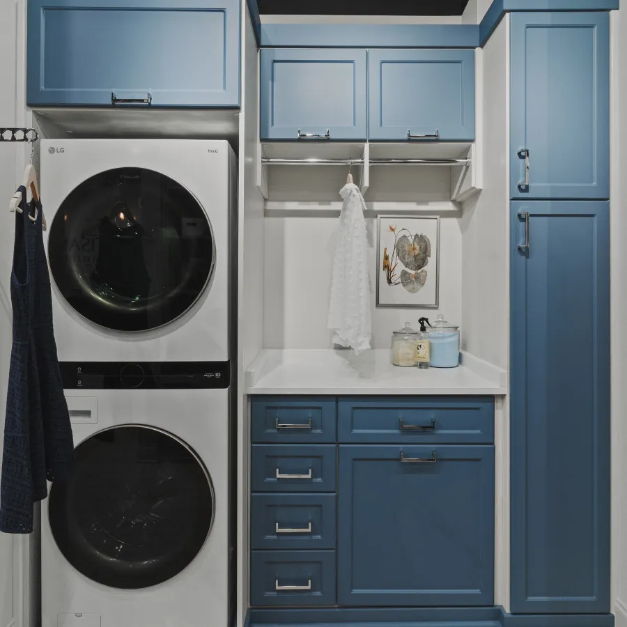 Modern laundry room with stacked LG washer and dryer, blue cabinets, white countertop, rod for hanging clothes and laundry supplies