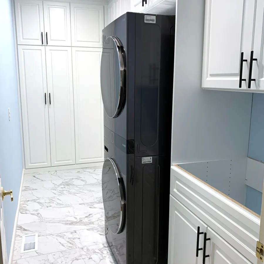 Modern laundry room with stacked black washer and dryer, white cabinets, and marble tile flooring.