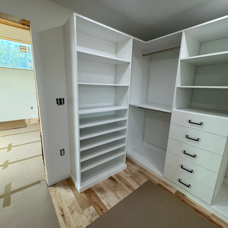 Newly installed white closet shelves and drawers in a room with wood floor and covered area.