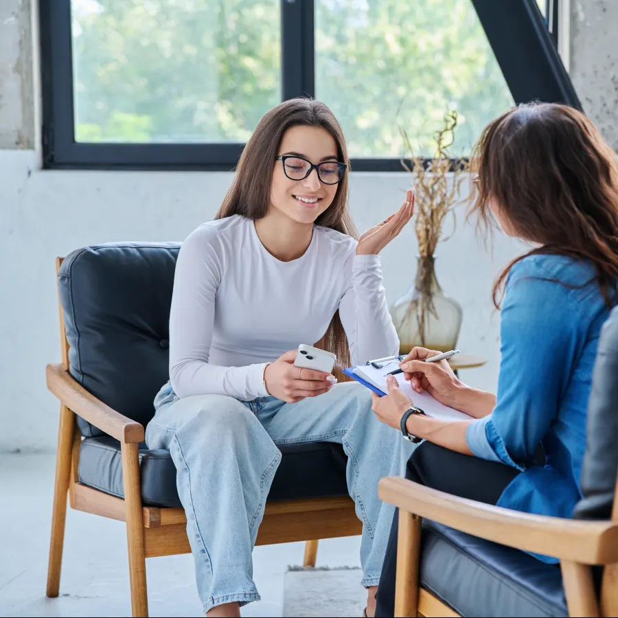 Worried young woman in blue sweater sitting and thinking during therapy session with female counselor