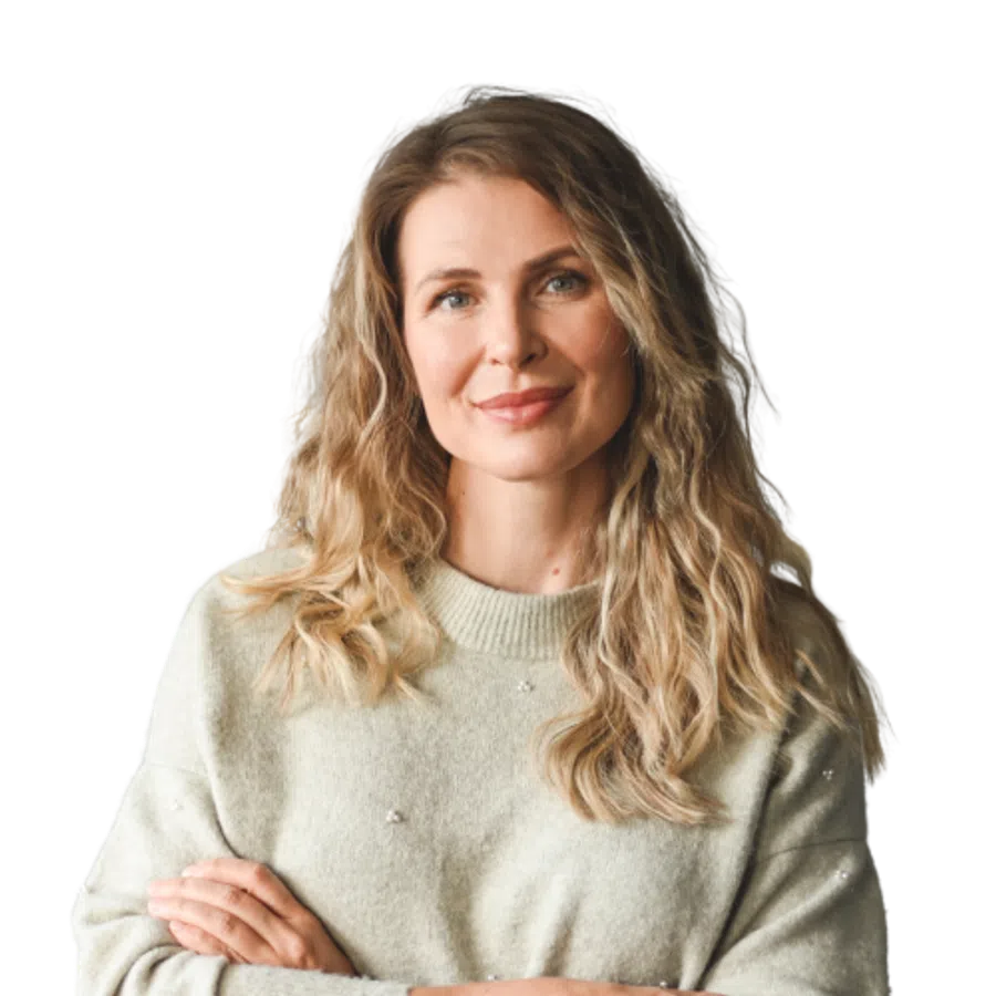 Smiling blonde woman with wavy hair wearing a light gray sweater with arms crossed confidently