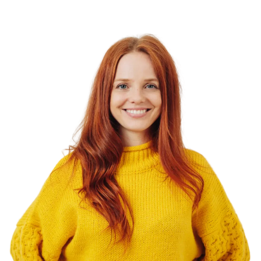 Smiling young woman with long red hair wearing a bright yellow knitted sweater posing with hands behind back.