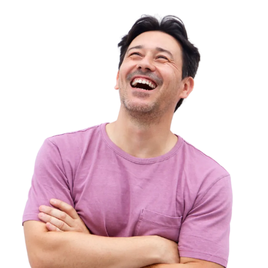 Man in pink t-shirt laughing joyfully with arms crossed and head tilted back.