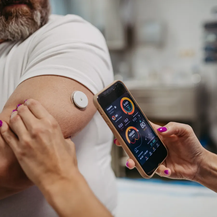 Person using a smartphone app to monitor health metrics from a wearable sensor on their upper arm.