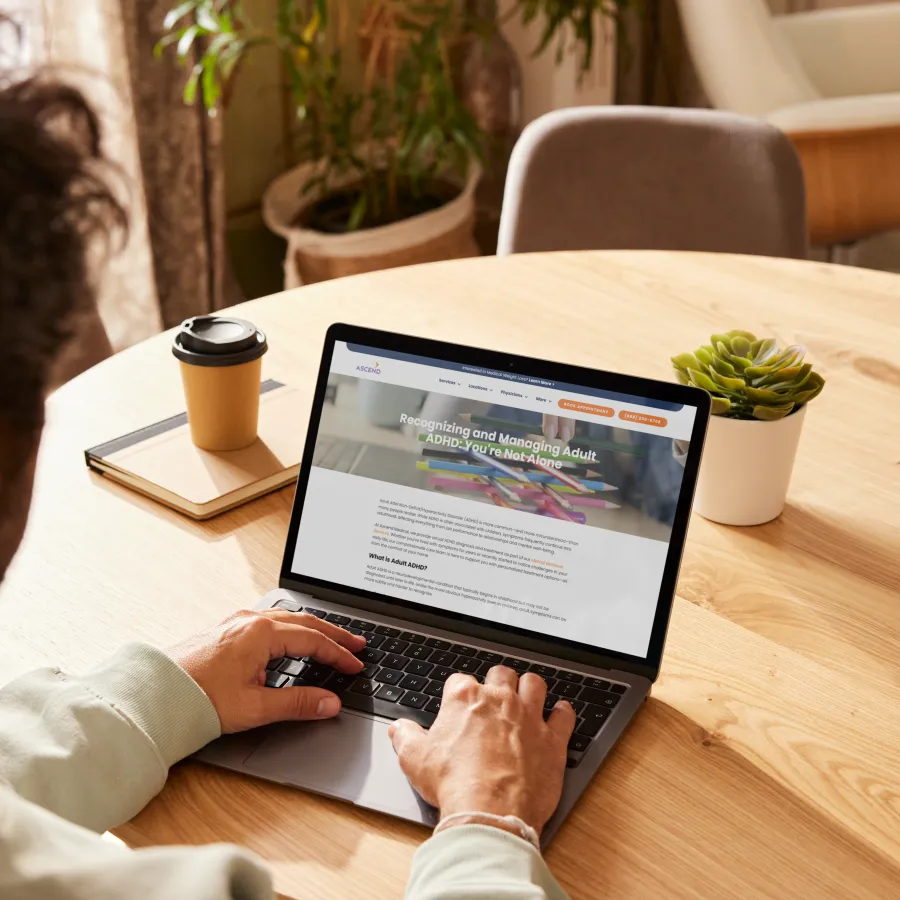 Person using laptop at wooden table viewing a webpage about recognizing and managing adult ADHD.