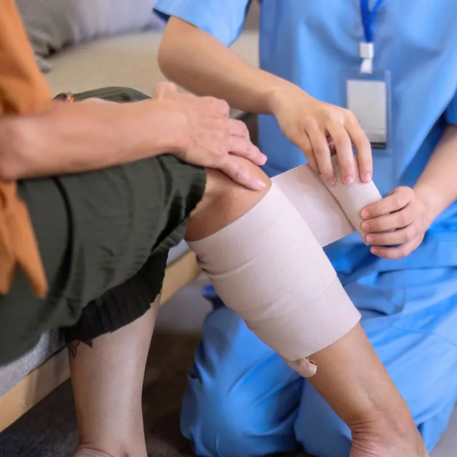 Healthcare professional wraps compression bandage around patient's injured knee during treatment session.