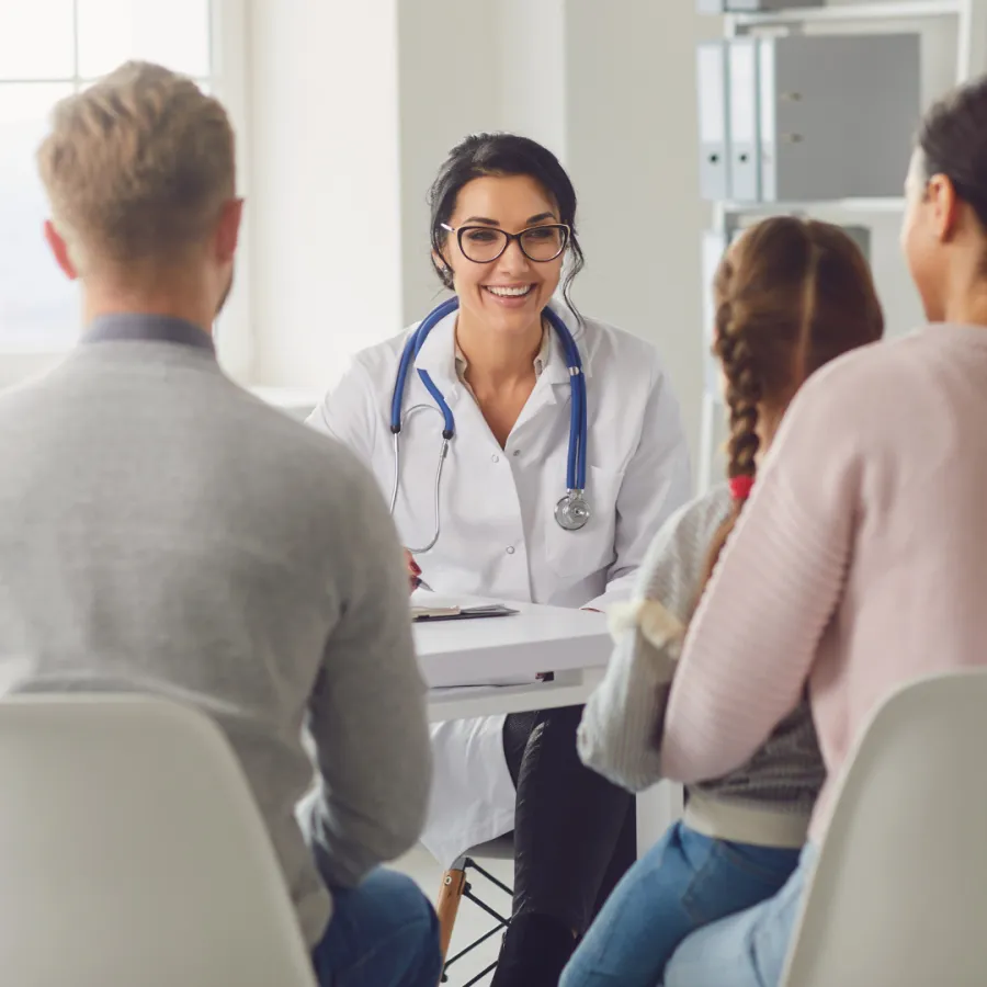 Smiling female doctor with stethoscope consulting with a family of three in a bright medical office.