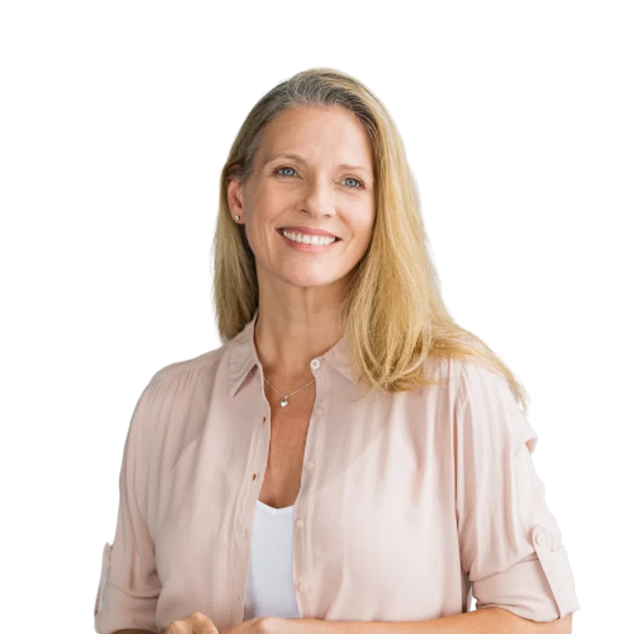 Smiling middle-aged woman with blonde hair wearing a light pink shirt and white top, posing with hands clasped.