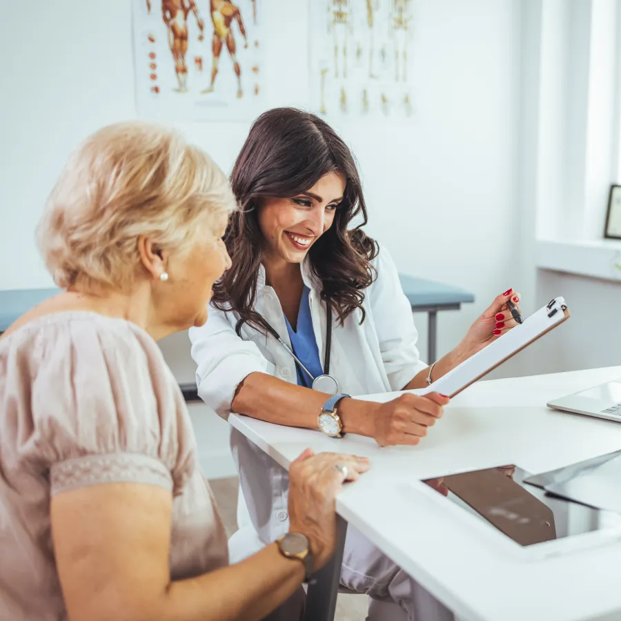 A doctor consults with an elderly patient in a bright, modern clinic office.