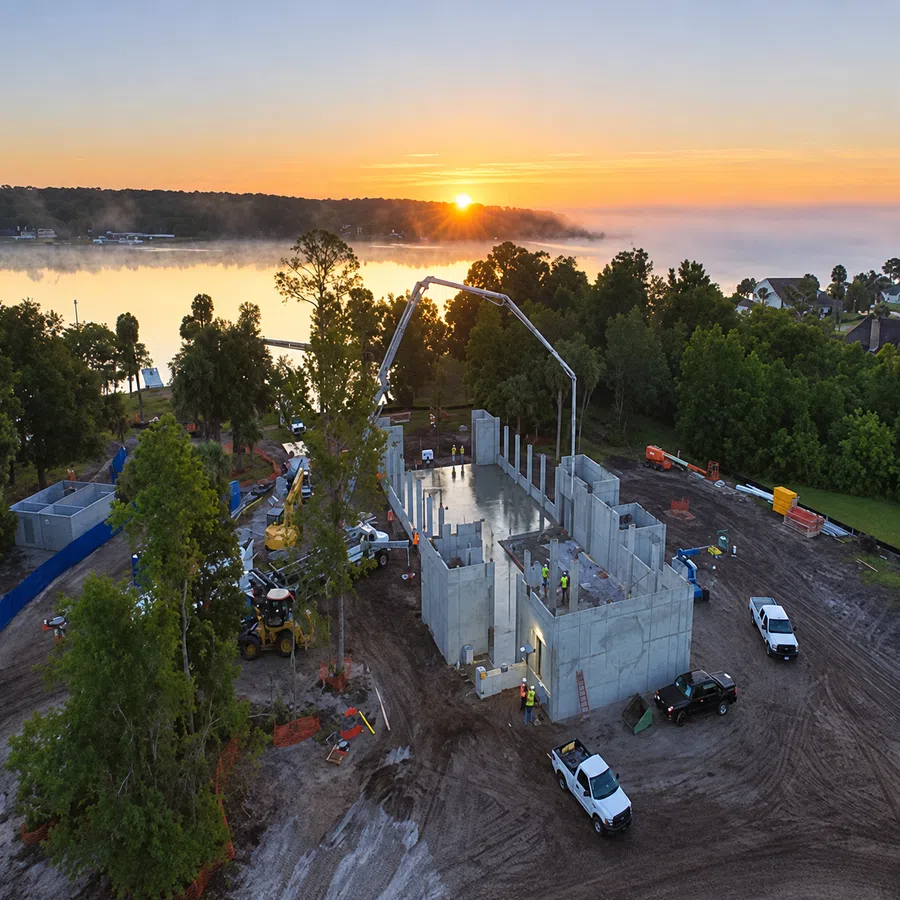 Sunset over a lakeside construction site with concrete walls, workers, and machinery in progress.
