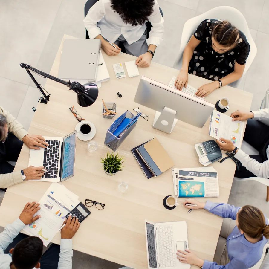 Top view of a diverse team collaborating around a modern office desk with laptops and documents.