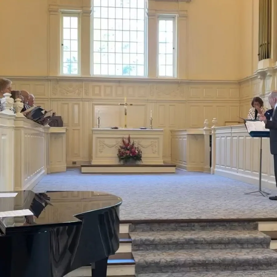 Choir singing in a church sanctuary with grand piano and altar in natural light from large windows