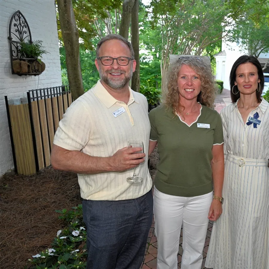 Four adults smiling outdoors at a social event in a garden setting, dressed in business casual attire.