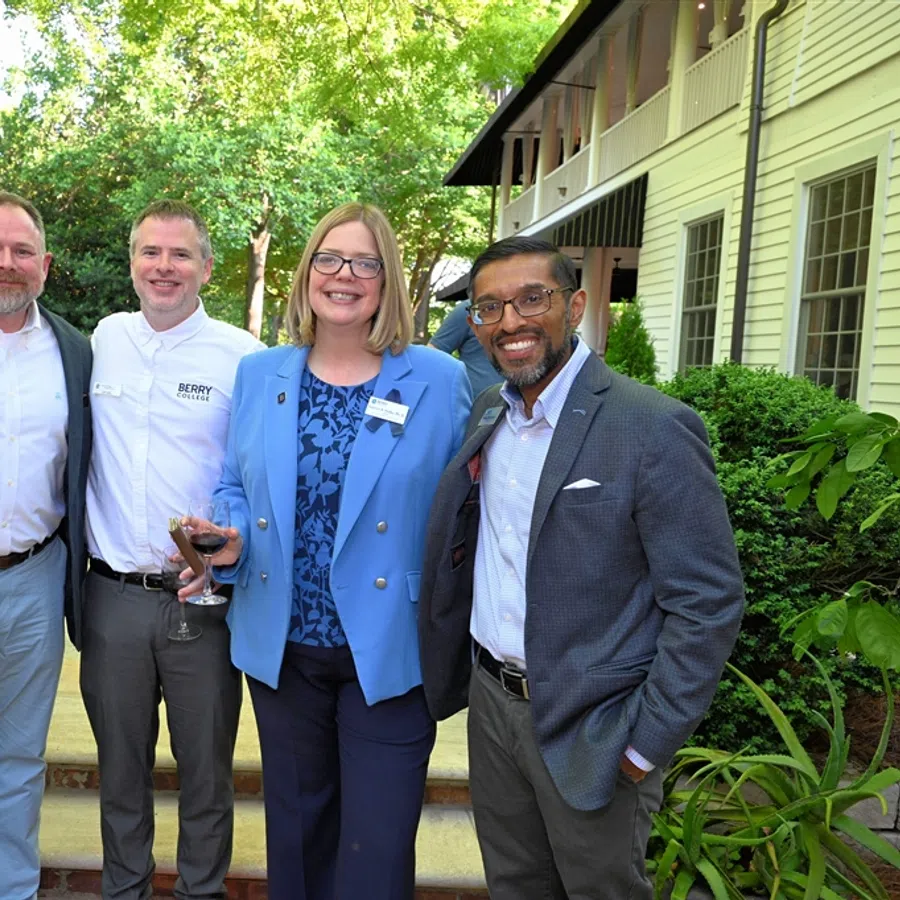 Four professionals smiling outdoors in business casual attire at a garden event on a sunny day