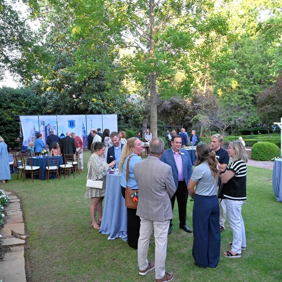 Outdoor garden networking event with people socializing near cocktail tables and greenery in the background.