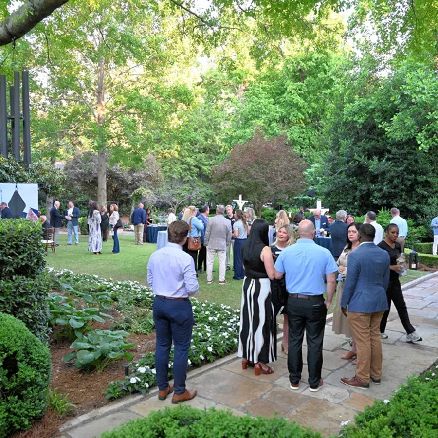 People socializing in a lush garden park with well-maintained greenery and paved walkways on a sunny day
