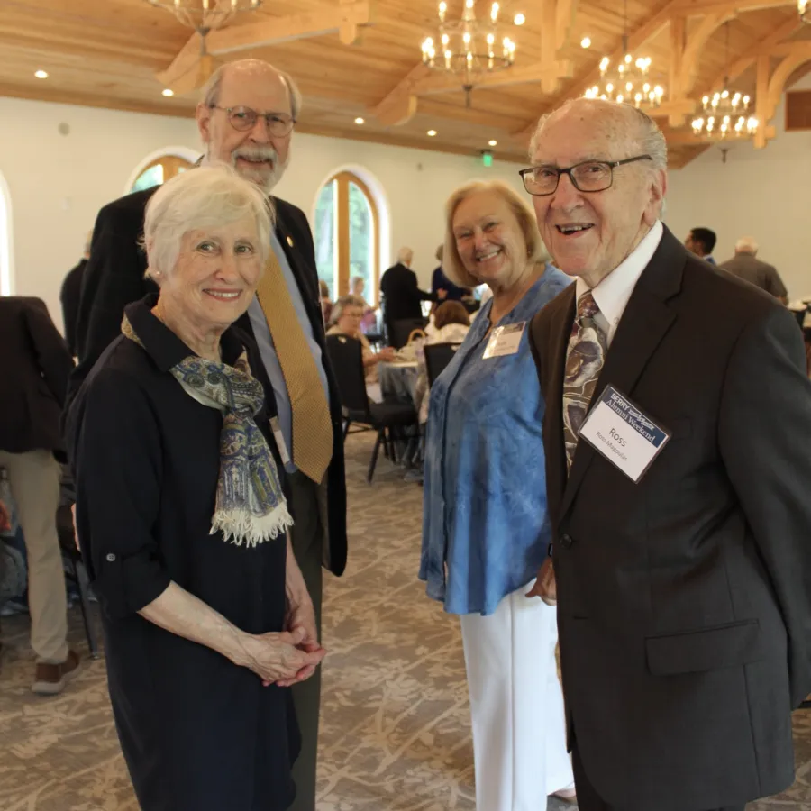Group of well-dressed older adults smiling and posing in a warmly lit, elegant event space with chandeliers.