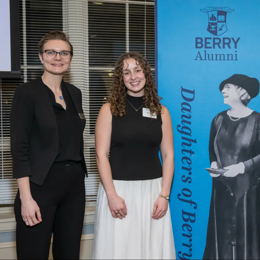Three women standing by a blue Berry Alumni Daughters of Berry banner at an indoor event