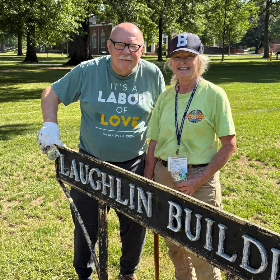 Two people stand outdoors near a Laughlin Building sign on a sunny day with green grass and trees.