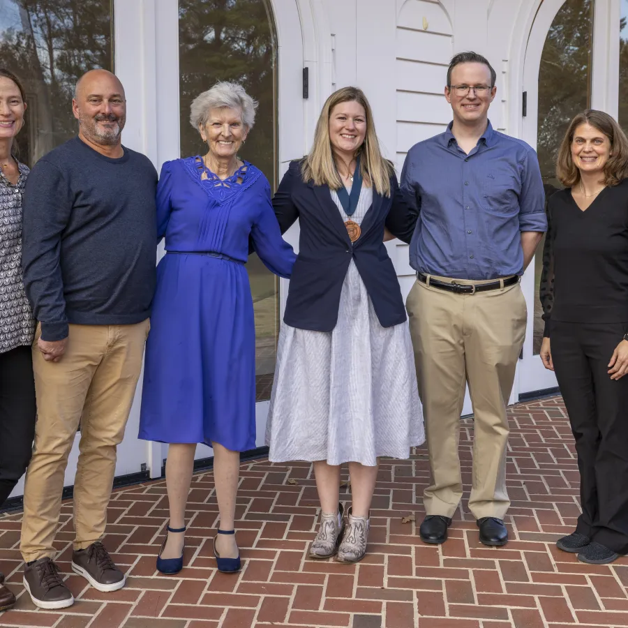 Group of seven professionally dressed adults posing outside a white building with glass doors on a brick patio.