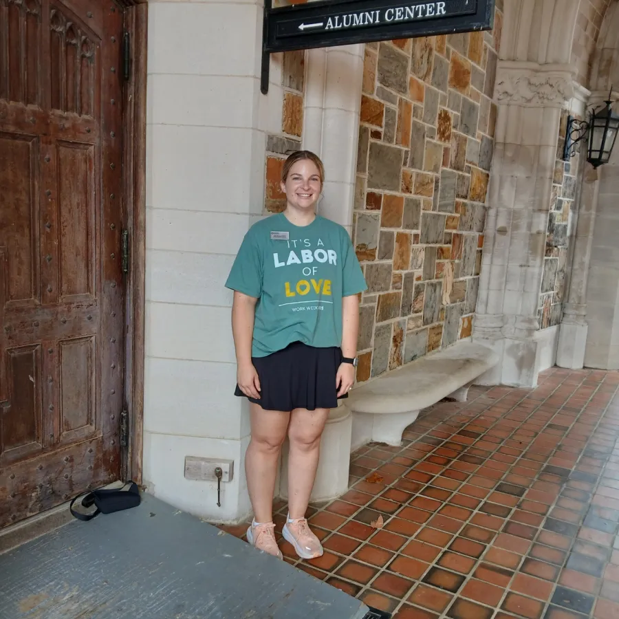 Young woman in casual outfit standing at entrance of stone building with Alumni Center sign overhead