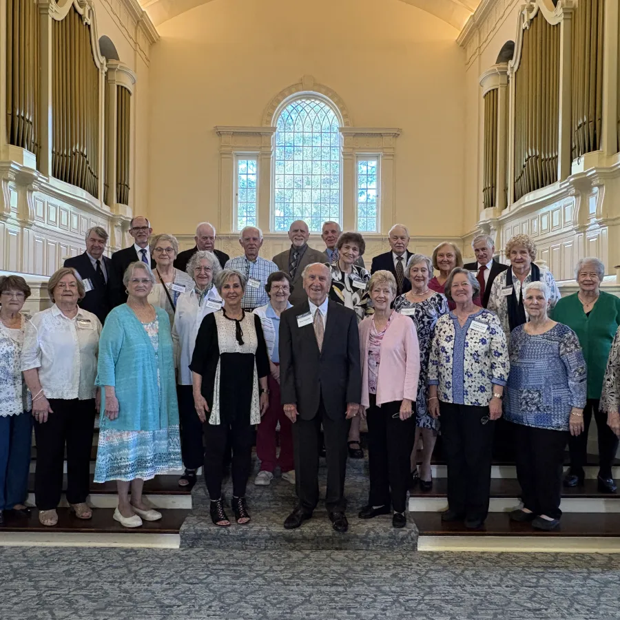 Group of seniors posing inside a church with stained glass window and organ pipes in the background