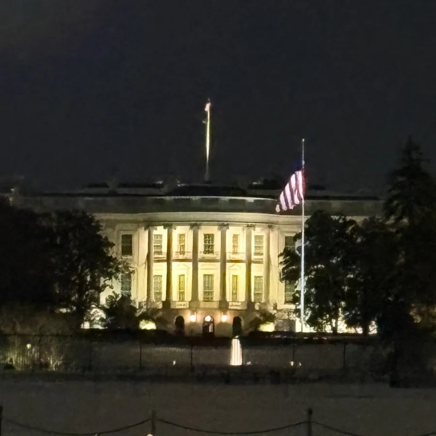 The White House illuminated at night with the American flag flying in front and snow on the ground.