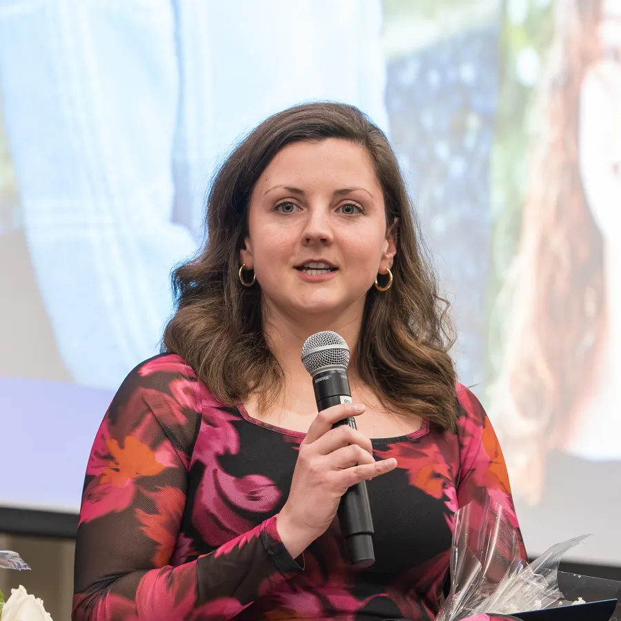 Woman in floral dress speaking into microphone during event or panel discussion