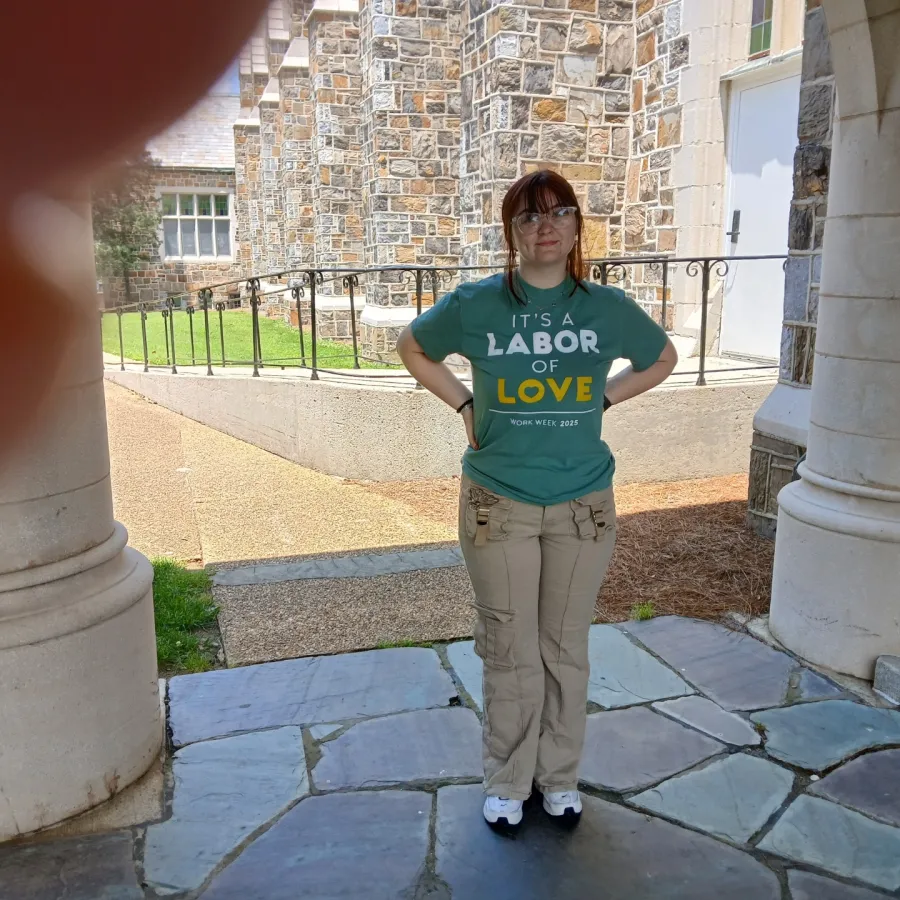 Young woman wearing a teal shirt with text standing between stone columns in an outdoor courtyard with stone pavement.