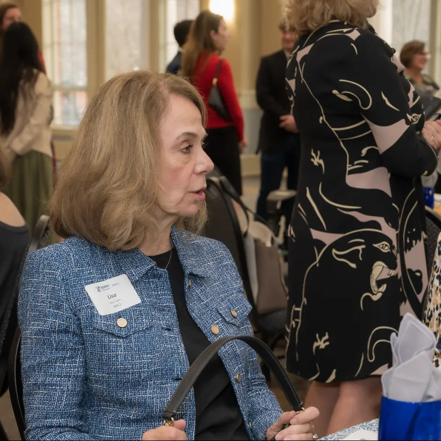 Two women with name tags engaged in conversation at a professional networking event with others in the background.