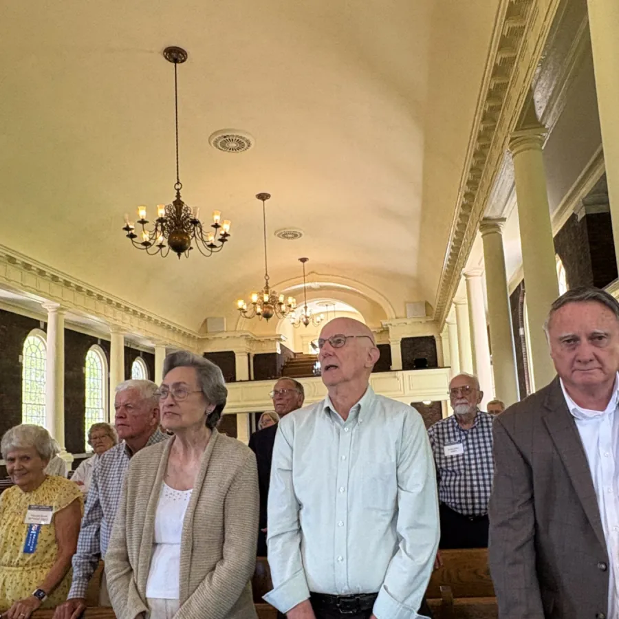 Group of older adults standing inside a historic building with chandeliers and stained glass windows.